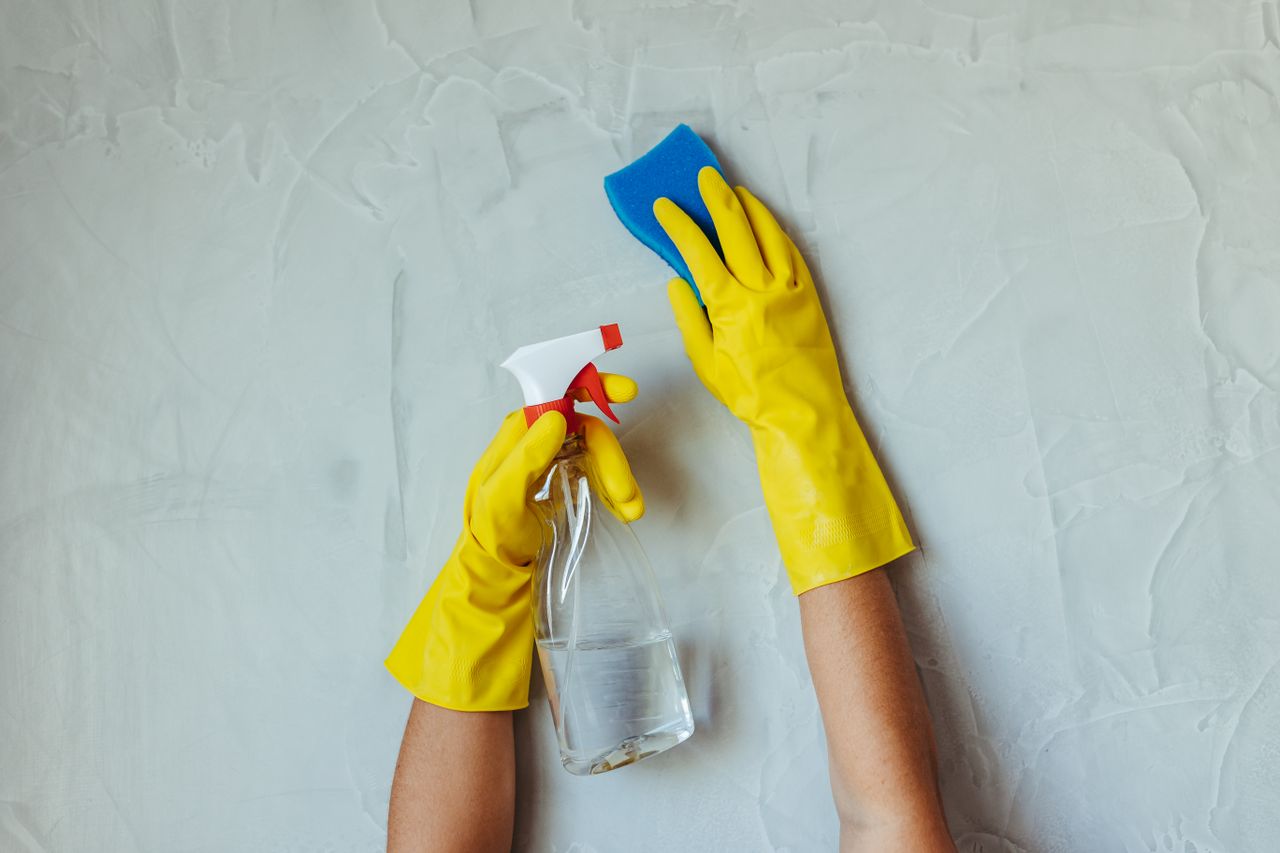 services-02 Close-up of hands in yellow gloves cleaning a wall with a spray bottle and sponge.